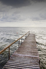 Obraz premium Wooden bridge on wavy lake. Dark sky before storm