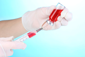 Syringe and medical ampoule in hands on blue background