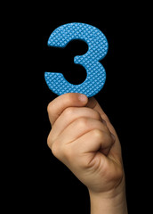Children hand holding the number Three