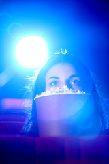 a pretty young woman sitting at theater, she is scared, and hide © stokkete