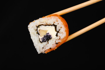 Holding roll with chopsticks isolated on black