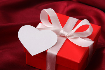 A gift with a red ribbon and heart on red silk