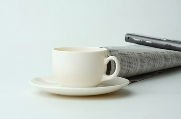 A cup of coffee, a mobile phone and a newspaper
