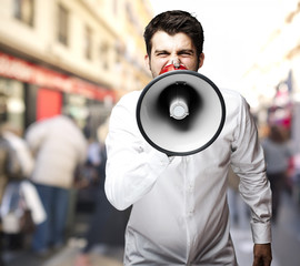 portrait of young man screaming with megaphone at city