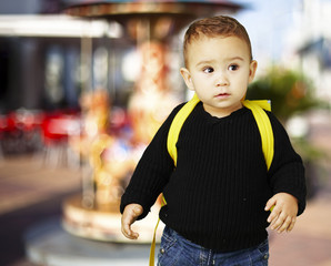 portrait of adorable kid carrying yellow backpack against a caro