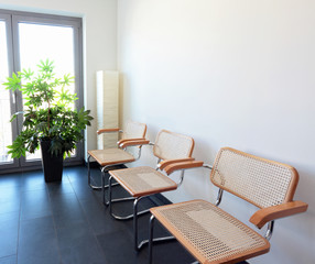Drei Stühle mit Stehlampe und Pflanze vor weisser Wand