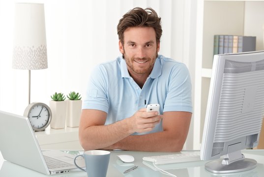 Smiling man at desk with mobile phone