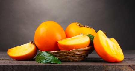 Appetizing persimmons in pad on wooden table on grey background