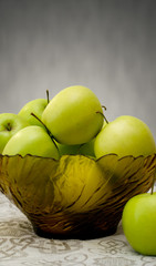 green apples in a glass vase on the table cloth