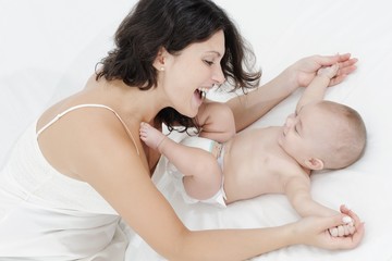 Mother and daughter playing happily on white bed
