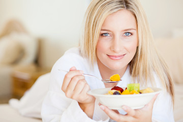 Obraz na płótnie Canvas pretty young woman eating breakfast fruit salad on bed