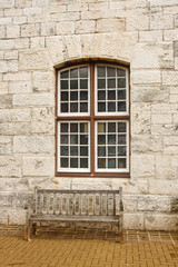 Fototapeta na wymiar Old Wooden Bench Under Window in Stone Block Wall