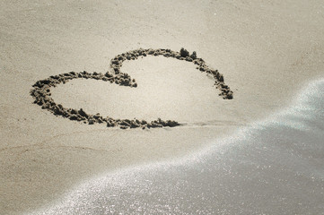 Handwritten heart on sand with wave approaching