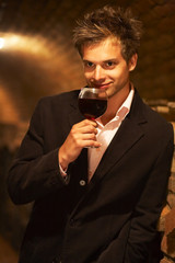 blond young man in a wine cellar,holds a wine glass in his hands