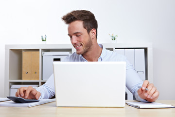 Mann am Laptop mit Taschenrechner
