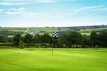 Obraz premium Golf green with a checkered flag, the countryside in background