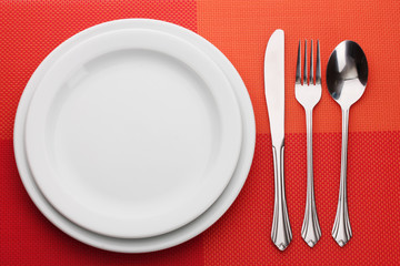 White empty plate with fork, spoon and knife on a red tablecloth