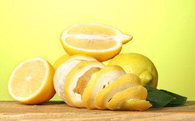 ripe lemons with leaves on wooden table on green background