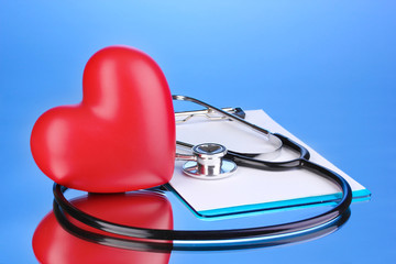 Medical stethoscope with clipboard and heart on blue background