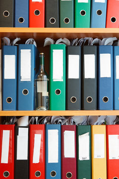 Glass bottle with alcohol hidden between file binders on shelves