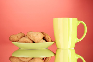 Heart-shaped cookies on plate and cup on red background