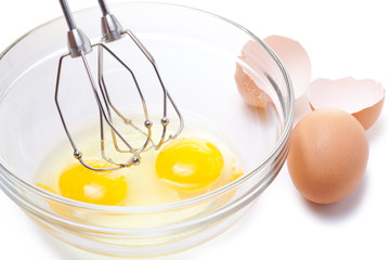 Wire whisk and brown eggs, isolated on white.