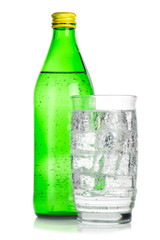 Green glass bottle and glass of mineral water with ice cubes