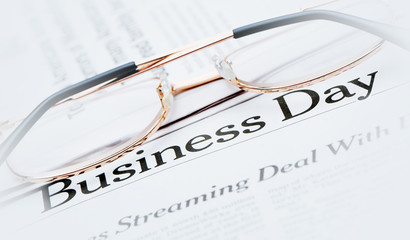 Eyeglasses lie on the newspaper with title Business day. Blue to