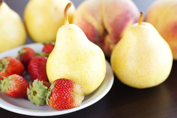 strawberry  in plate, pear and peach on a wooden table