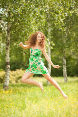 Naklejka na ściany i meble Young redhead woman jumping in the park with flowers