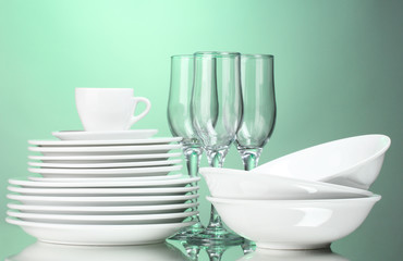 Clean plates, cup and glasses on green background