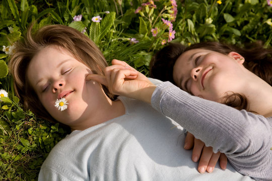 A girl with Down syndrome and her sister in the grass.