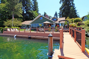 Lakefront green one story house with dock and large deck. - Powered by Adobe
