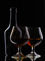 Glasses of brandy and bottle on black background