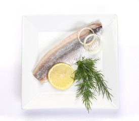 herring salt fillet with onion and lemon on white dish