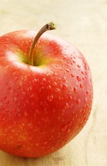 One large apple with drops of dew on the board