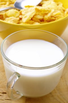 milk in a glass cup and corn flakes in a yellow bowl