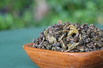 Wooden square bowl with dry leaf tea, shallow DOF