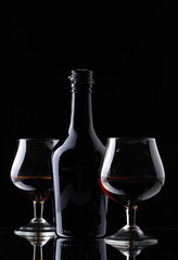 Glasses of brandy and bottle on black background