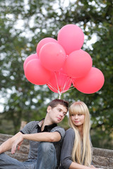 young couple with red balloons on natural background
