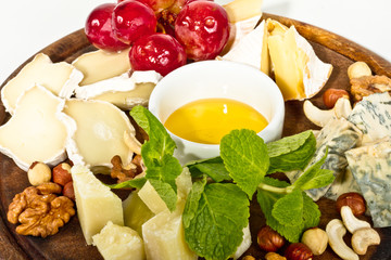 Various types of cheese with honey, nuts and grapes on plate, is