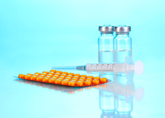 Syringe with medical ampoules and tablets on blue background