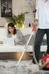 Man vacuuming and woman laid with laptop