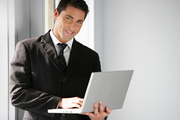 Man stood in office holding laptop