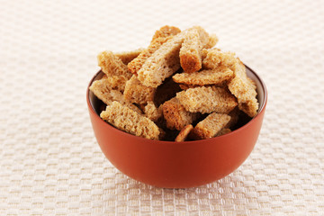 Appetizing rusks in bowl on beige napkin