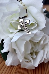 Rosenkranzkreuz halb verdeckt von Rosen weiß