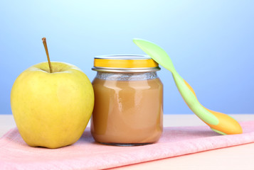 Jar of baby puree with spoon on napkin on blue background