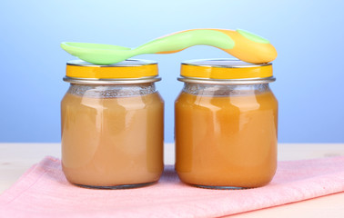 Jars of baby puree with spoon on napkin on blue background