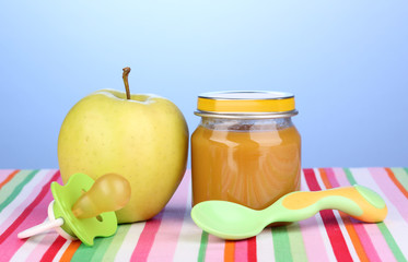 Jar of baby puree with spoon on napkin on blue background