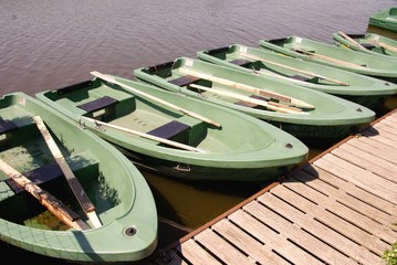 Green rowing boats in a row at a wooden jetty